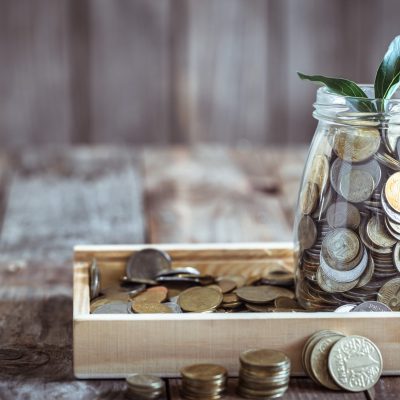 A jar with different coins and green growth growing from above, stand on a wooden background, the concept of growth and saving money